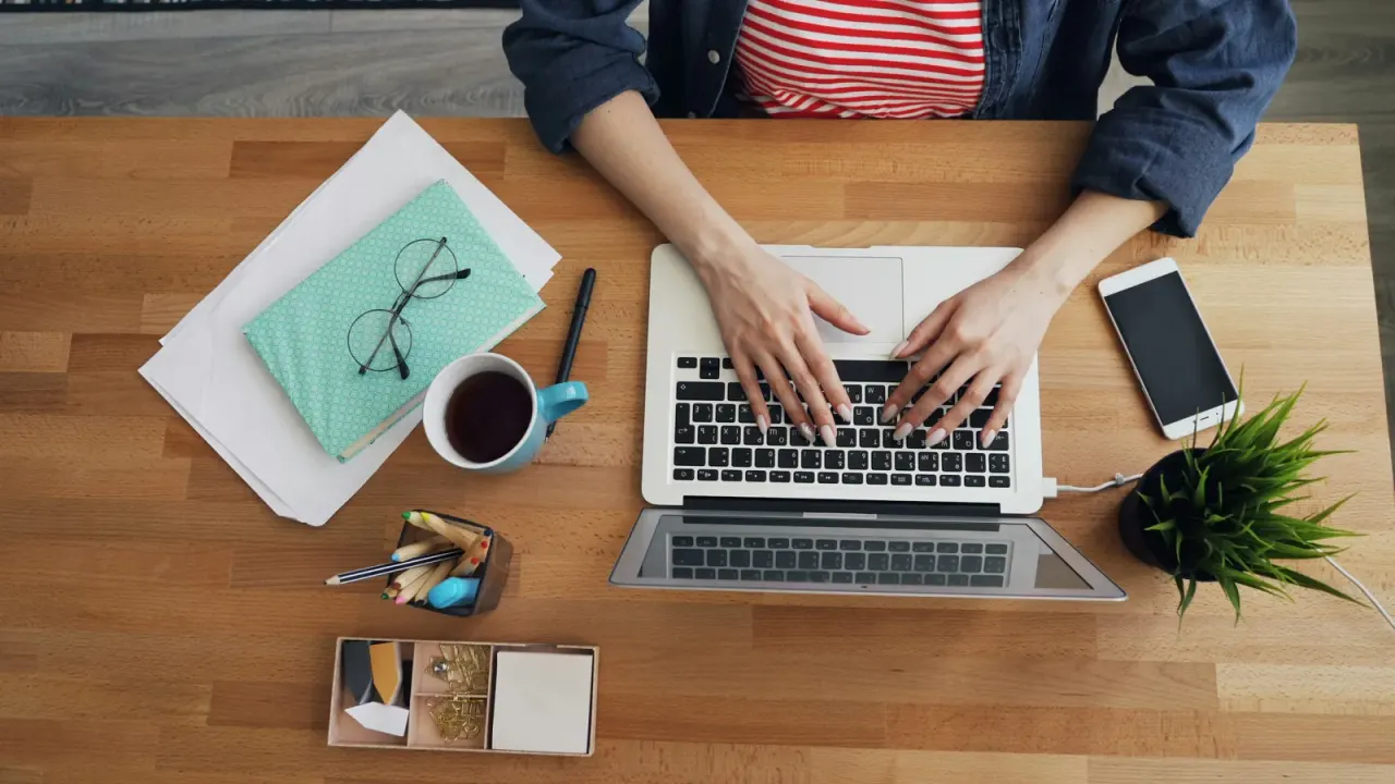 Person working on a laptop at a wooden desk during virtual addiction and mental health treatment