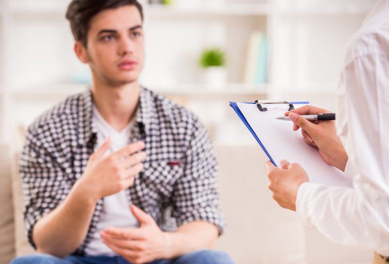 Depressed man talking to therapist while she taking notes.