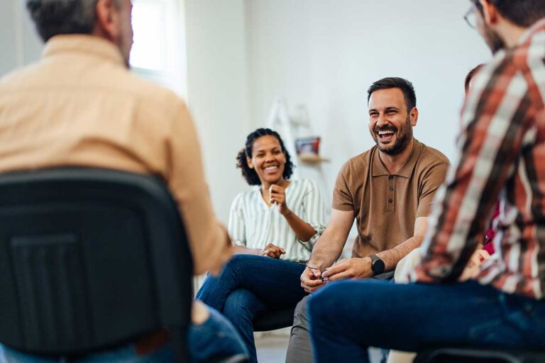 people smiling and laughing in group therapy while discussing group therapy vs individual therapy