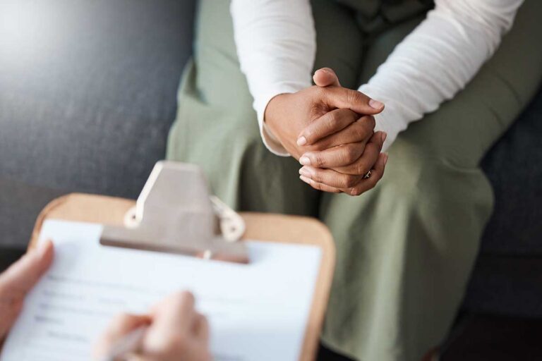 person with hands folded and clinician with clipboard during psychiatric assessment